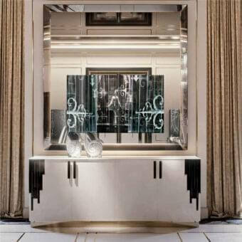 Horizontal cabinet with three doors sits beneath a framed mirror displaying a dark geometric pattern flanked by dark paneled walls