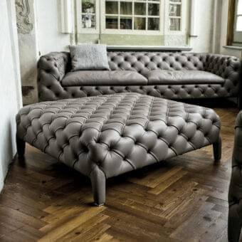 Gray square and rectangular forms with recessed indentations sit on a herringbone wood floor in a room corner