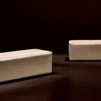 Stylish Rugiano Form ottoman upholstered in light beige textile with subtle piping and refined steel finish