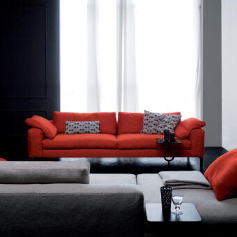 Orange Molvedo sofa with rounded arms, black and white pillows, and adjacent gray modular sectional in a modern living room.