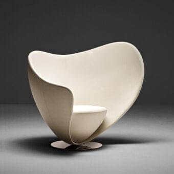 Off-white curved form with recessed interior rests on a dark circular base against a gray background