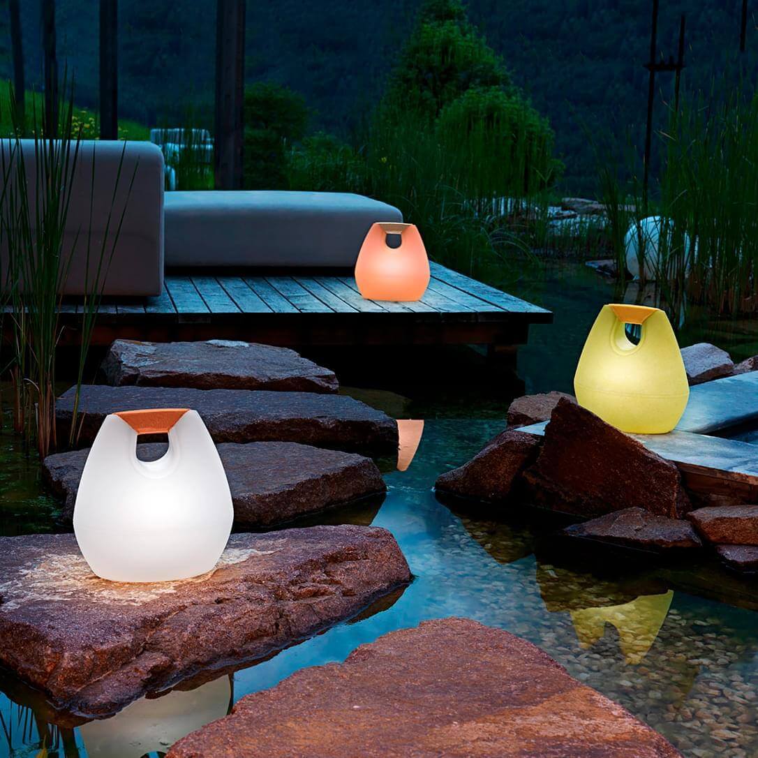 Sculptural lamps in pale white, yellow, and orange illuminate rocks and water, featuring organic vessel shapes and wooden accents.