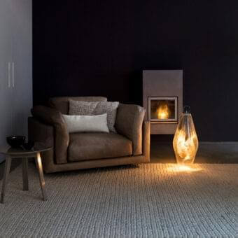 Light brown upholstered seating with patterned cushions beside a gray vertical panel and dark table with a bowl shaped object