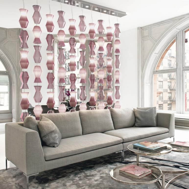 Modular gray sofa with square arms, set before mirrored coffee tables, and a backdrop of suspended translucent pink glass orbs in a modern interior.