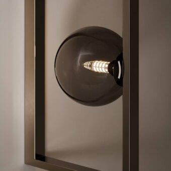Mondrian glass wall lamp, smoky gray oval shade, dark metal frame, visible filament bulb, vertical ribbed glass, warm golden light.
