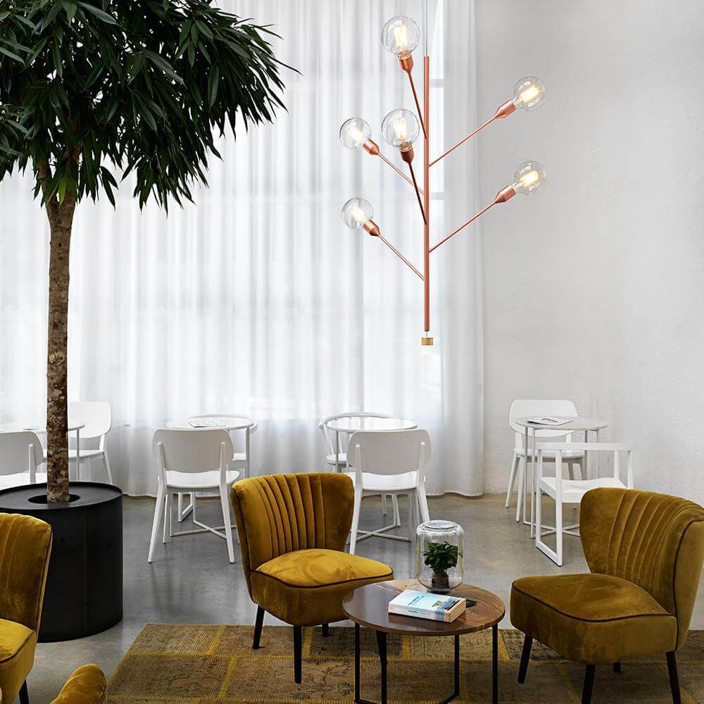 Copper floor lamp with glass globes illuminates modern lounge with yellow velvet armchairs, white tables, and concrete floor.