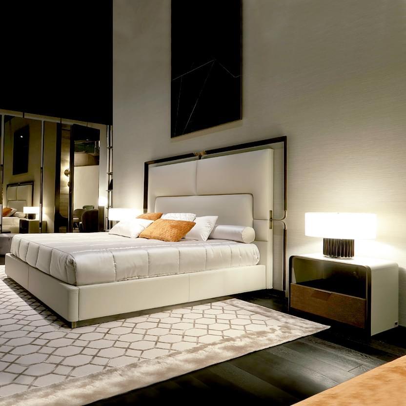 King bed with beige upholstered headboard, vertical tufting, rust pillows, wood nightstand, and geometric Rugiano rug on dark wood floor.