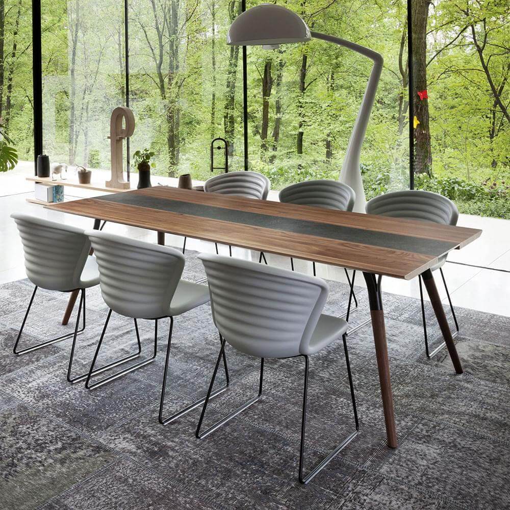 Walnut dining table with light gray epoxy resin inlay, six gray ribbed chairs, and arched floor lamp in a modern dining room.