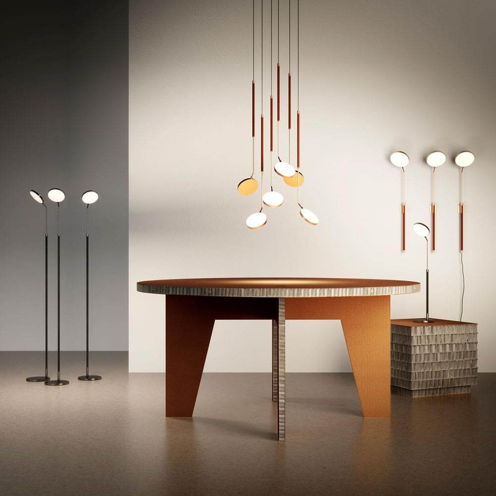 Penta floor and pendant lights with copper rods and white shades illuminate a round reddish-brown wood table with A-frame base.