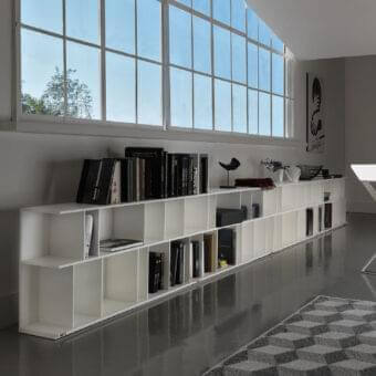White stepped shelving units stretch across a gray floor against a pale wall beneath a grid of rectangular windows
