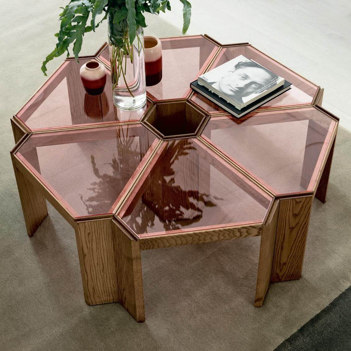 Hexagonal coffee table with rose acrylic top and light wood frame, styled with vase, ceramics, and books on a gray rug.