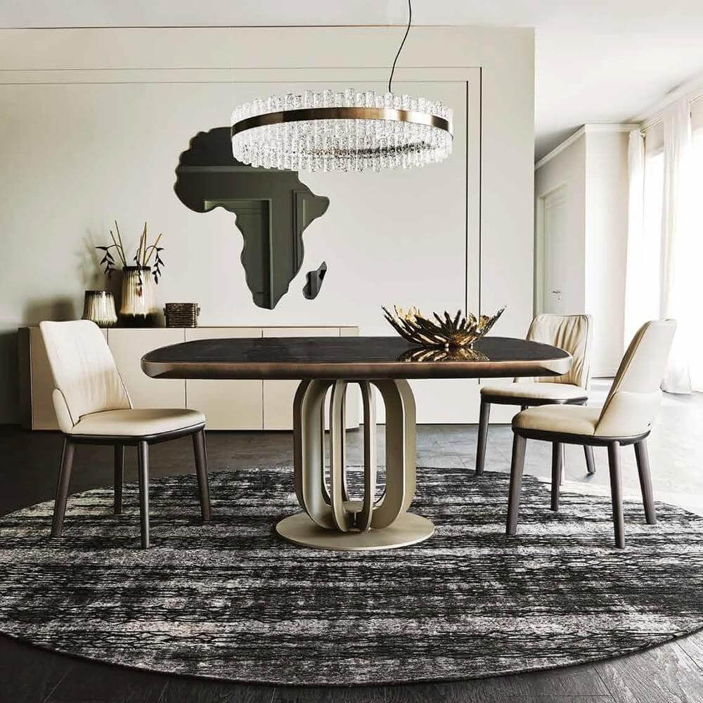 Dining table with dark wood top and champagne metal base, surrounded by beige fabric chairs, under a crystal chandelier.