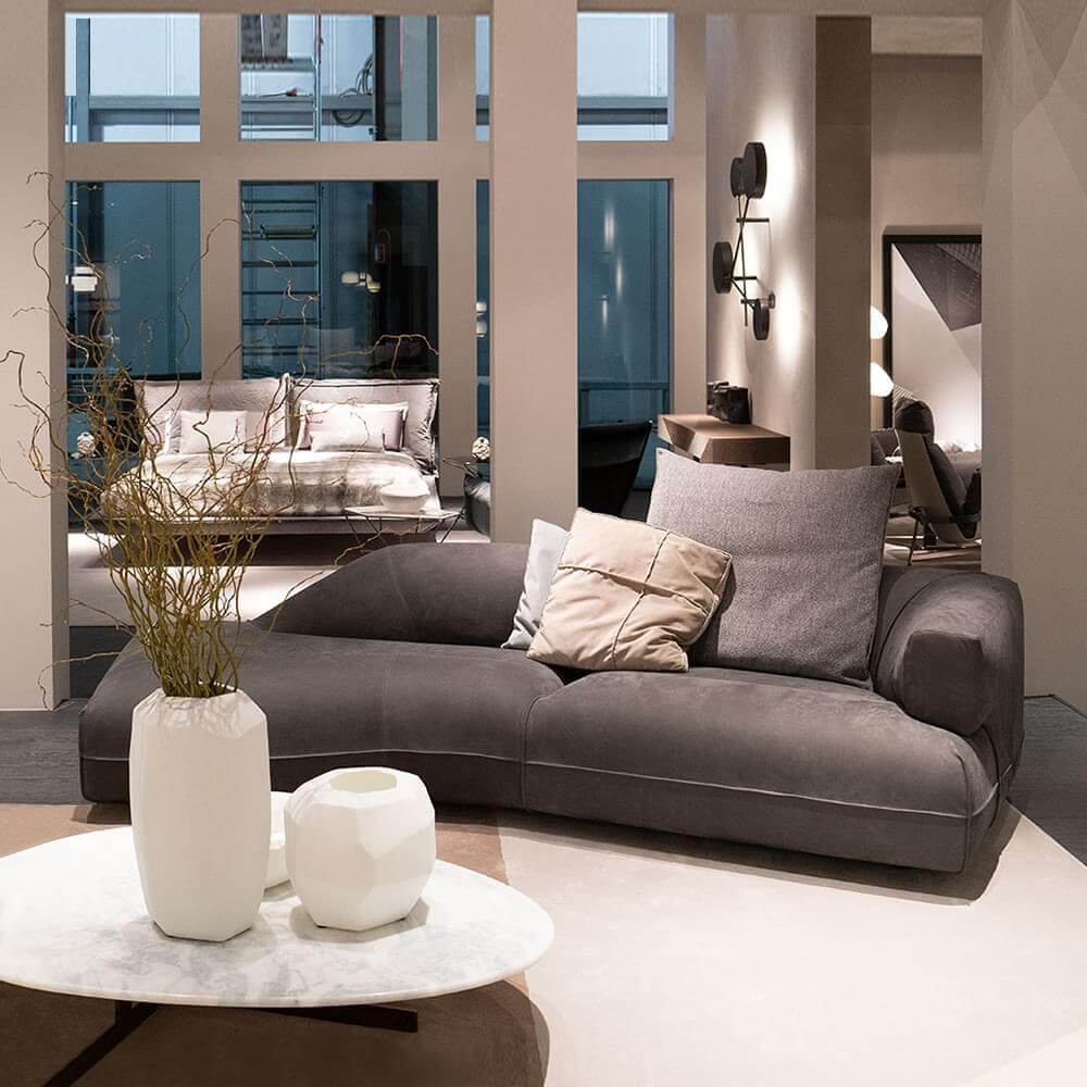 Gray sofa with textured upholstery, square pillows, white marble coffee table, dried branches in ceramic vases, teal windows.