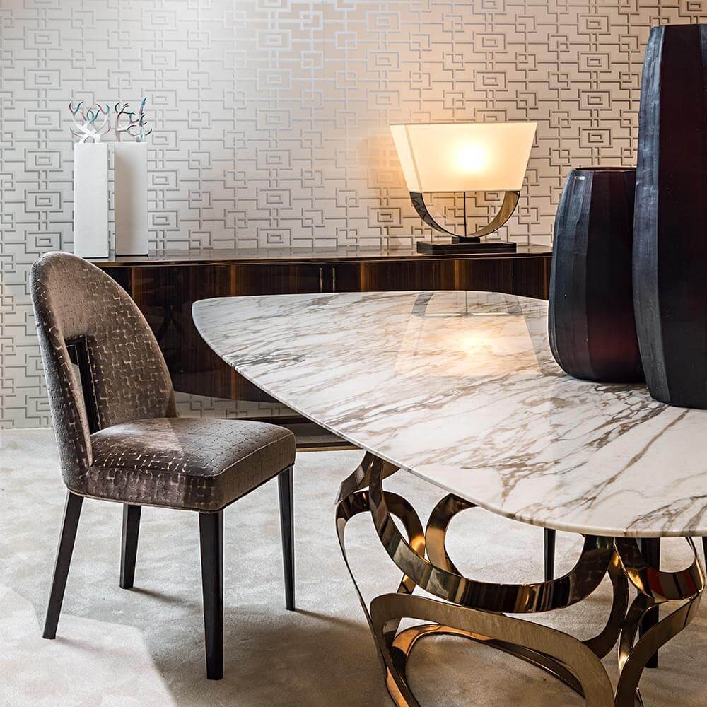 White marble dining table with silver metal base, cream lamp, brown fabric chair, dark wood console, geometric wallpaper, grey vase.