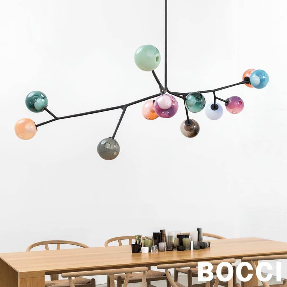 Bocci chandelier with black metal frame and multi-colored glass orbs hangs over a wooden dining table in a studio setting.