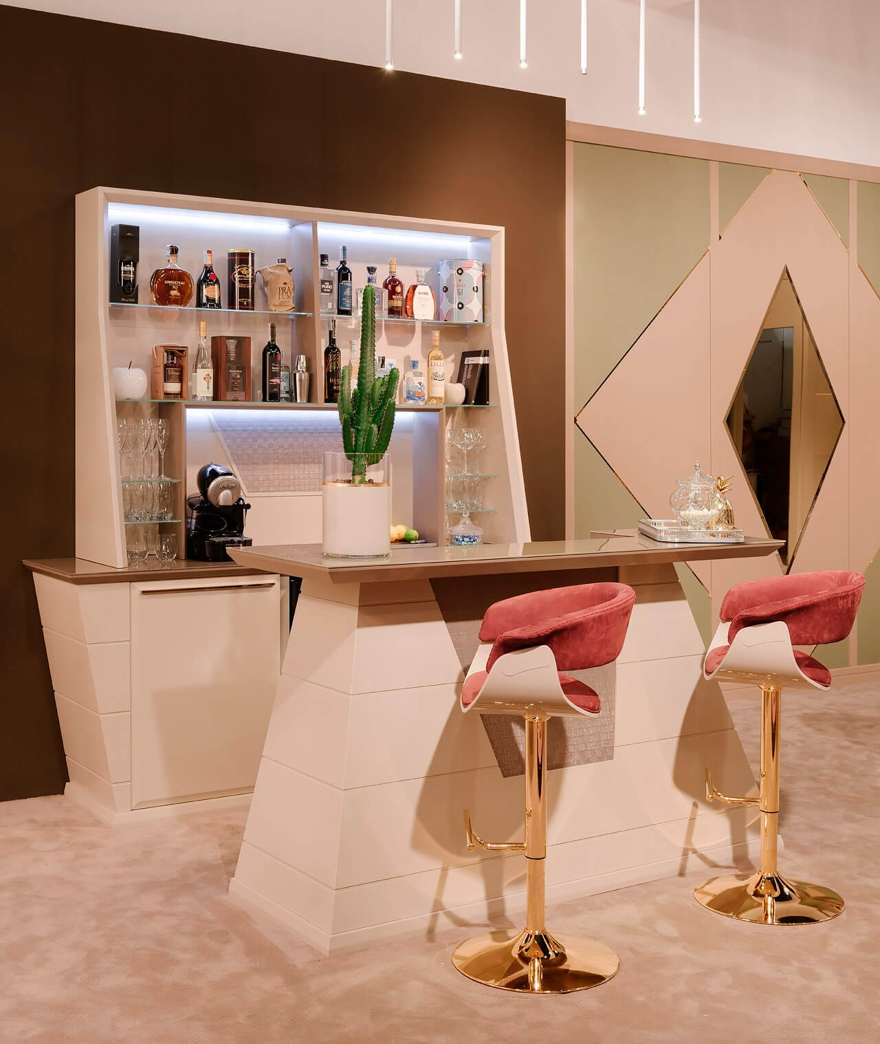 Home bar with white geometric design, stepped counter, and integrated shelving displaying liquor bottles and glassware, with rose velvet stools.