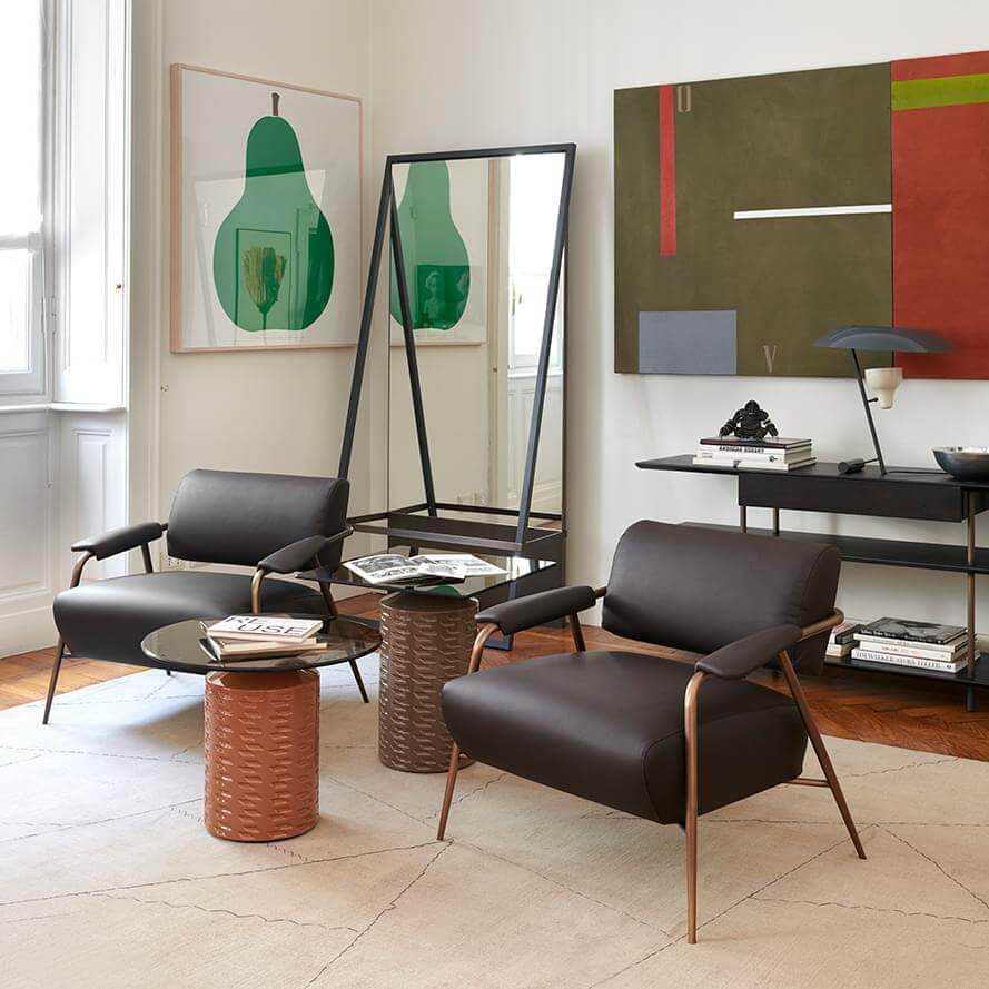 Black leather armchairs with bronze side table, mirror, and green abstract painting in modern cream interior.