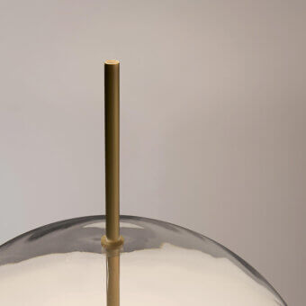 Table lamp, silvery-gray metal shade, slender brass stem, circular fitting, studio lighting, neutral gray background, reflective glossy surface.