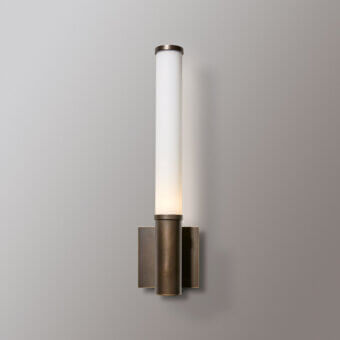 Venicem wall lamp, white glass shade, bronze metal fixture with layered cylindrical elements and brushed patina finish against a light gray wall.