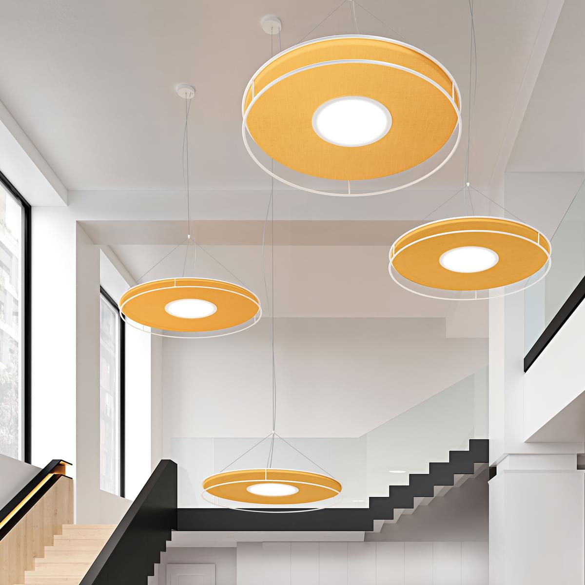 Circular pendant lights, yellow fabric shades, diffused glow, modern interior with white walls, black staircase, transparent cords.