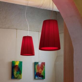 Red pleated conical shades hang from cables before a wall displaying two framed portraits and a text-based artwork