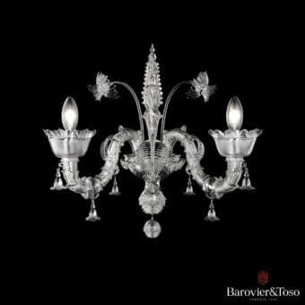 Symmetrical glass fixture with branching supports, cup-shaped forms, and a central elongated element against a dark backdrop
