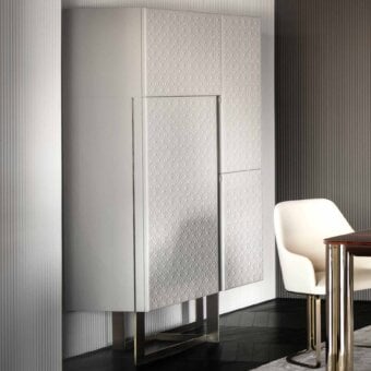 Tall cabinet, light gray, diamond texture, with brass X-base; against ribbed gray wall and modern chair/table setting.