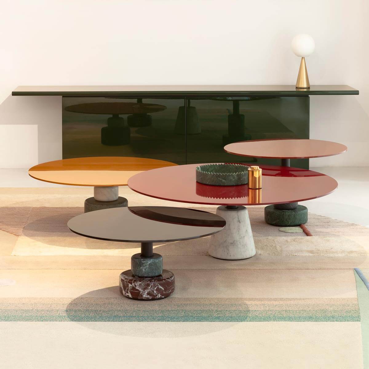 Circular coffee tables in red, gold, gray & brown with marble bases, a dark green sideboard, and a brass lamp on a beige rug.
