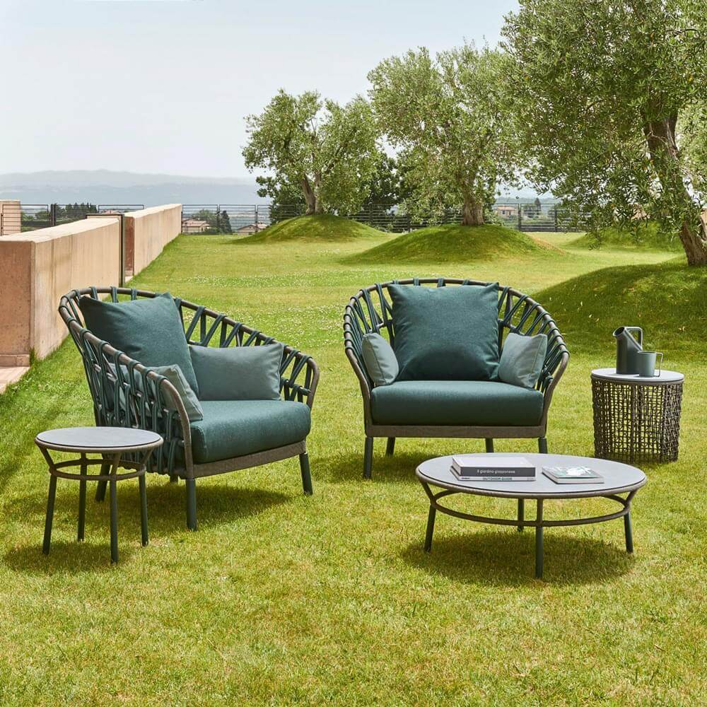 Outdoor furniture set with dark green woven fabric, black metal frames, rounded armchair, sofa, side & coffee tables, garden setting.