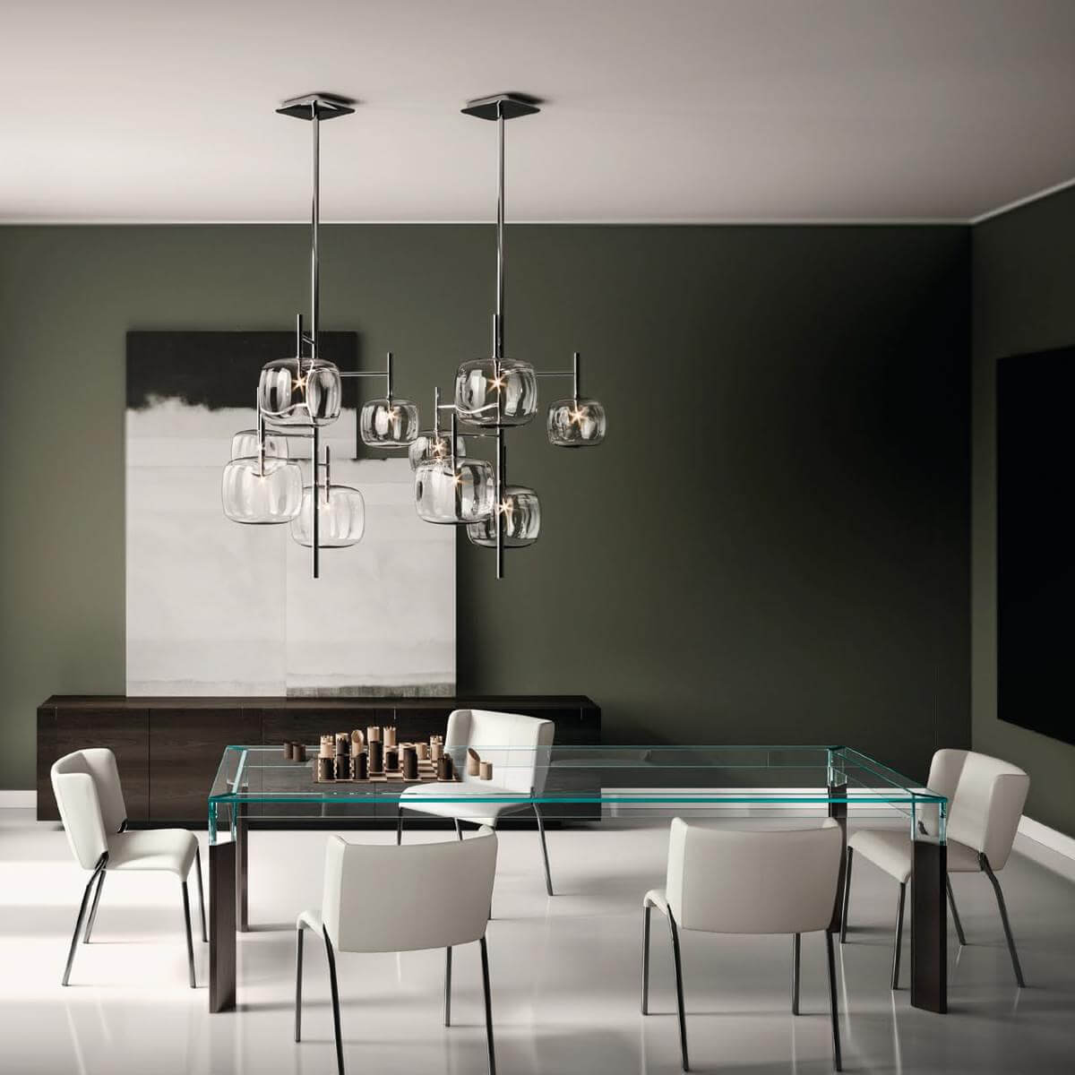 Glass dining table with six white chairs, silver frames, and walnut base, under a multi-tiered glass orb chandelier in olive green dining room.