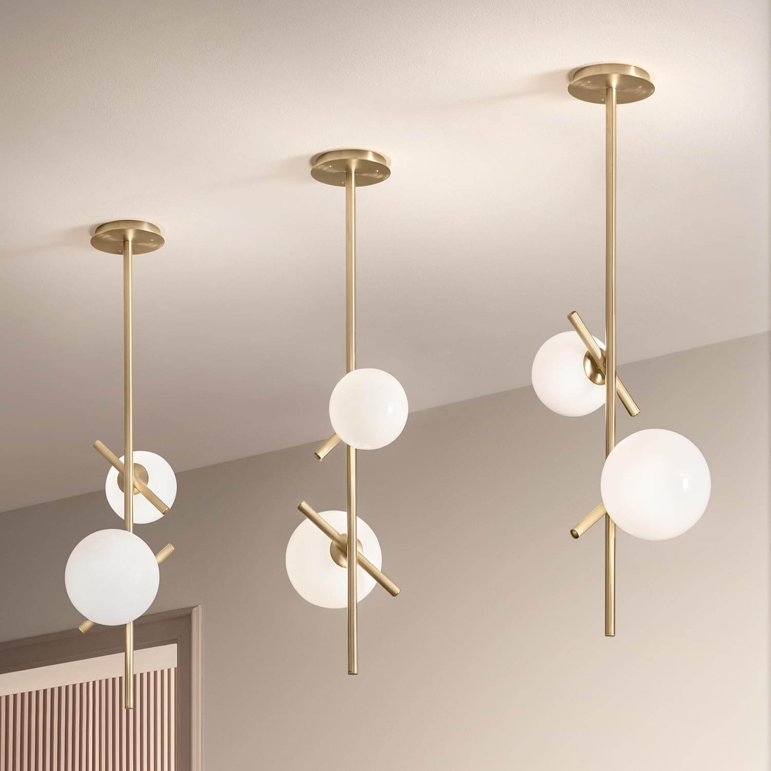Pendant lights, brushed brass and opaque white glass, circular globes with intersecting rod detail from Masiero 2022 collection.