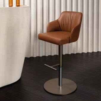 Superior Reflex Comfort stool in warm brown leather with brushed bronze metal base and curved silhouette