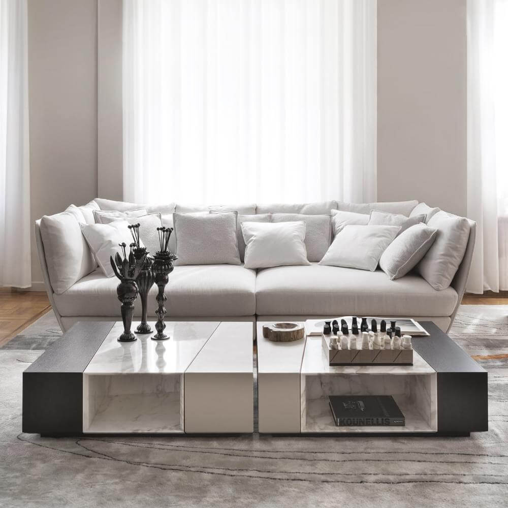 Modular sofa light gray fabric, rounded armrests, with marble coffee table, dark wood base, chess set, and metal sculptures.