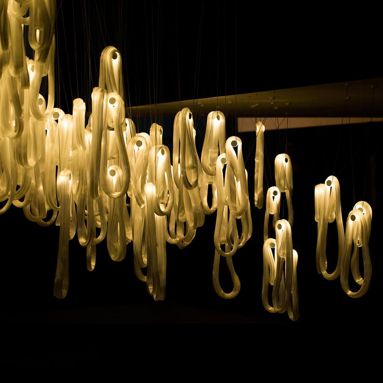 Pale yellow translucent forms are vertically suspended with dark lines against a dark background creating depth