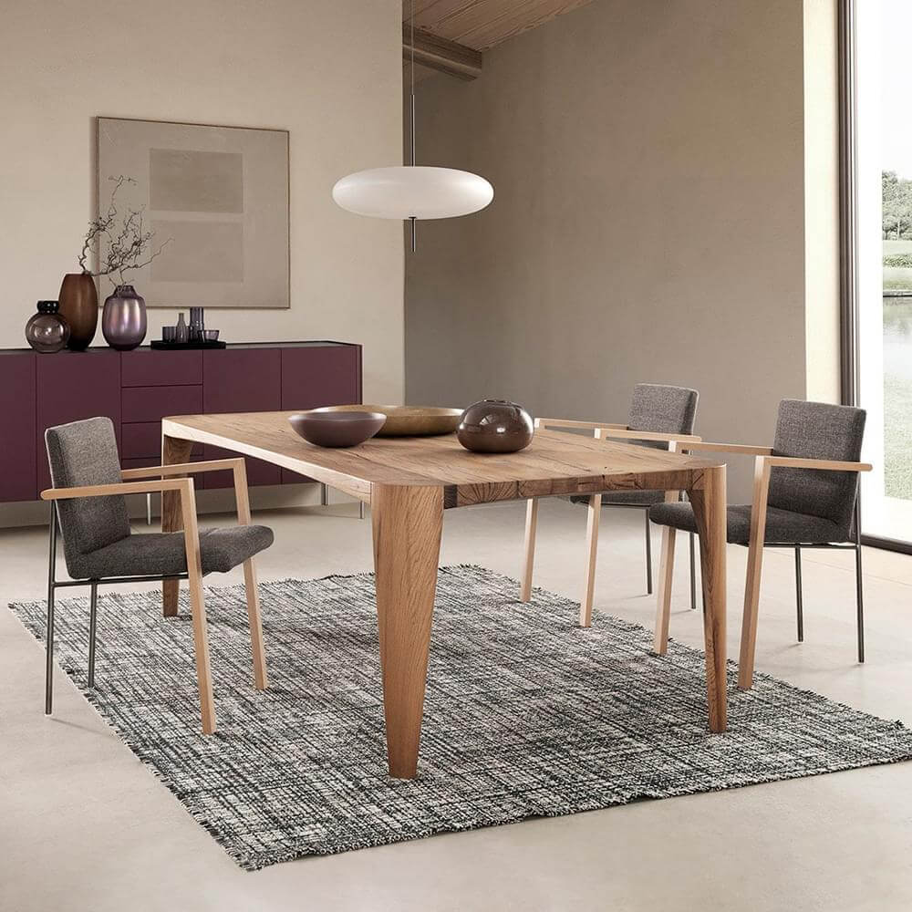 Rectangular wood dining table with four gray upholstered armchairs on a textured rug, plum sideboard, and white pendant light.