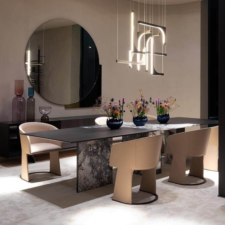 Dining table with gray marbled stone, six beige chairs, and white rectangular chandelier over beige rug in contemporary room setting.