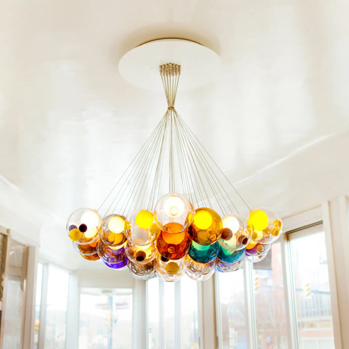 Bocci 28 chandelier with hand-blown glass orbs in amber, teal, purple, and clear glass, suspended from silver wires on a white ceiling mount.