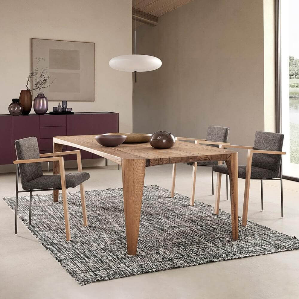 Rectangular wood table with four chairs sits on a woven fiber rug before a plum cabinet and wall-mounted neutral panel