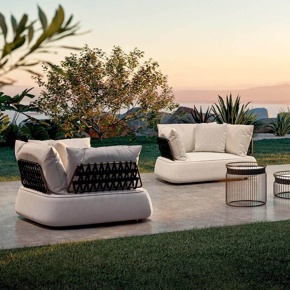 Outdoor sofas with cream upholstery and dark brown woven frames are arranged on a gray tile patio with gold side tables.
