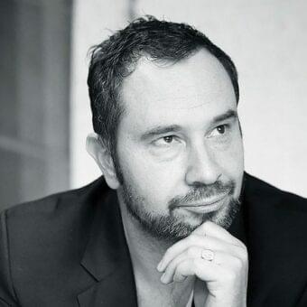 Grayscale portrait of a man with short dark hair and beard looking upwards, hand gently touching his chin