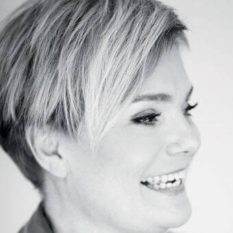 Monochrome portrait of a woman facing right with short hair, a slight smile, and upward gaze against a light gray background