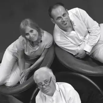 Three people are seated and positioned in a triangular arrangement against a plain gray background in grayscale