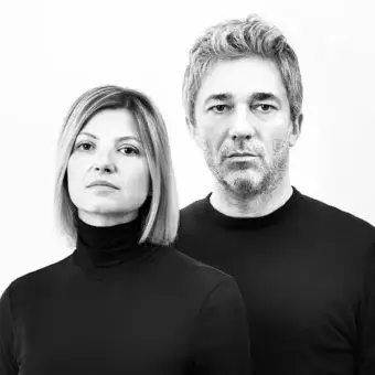 Monochromatic portrait of two people facing forward with dark clothing against a light gray background