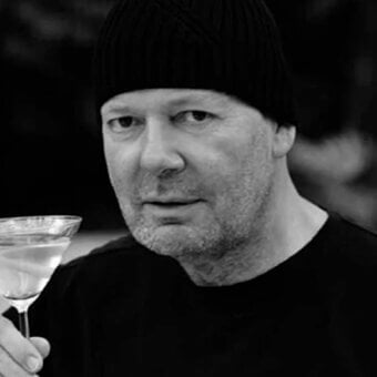 Gray scale portrait of a man with facial hair holding a stemmed glass against a blurred dark background
