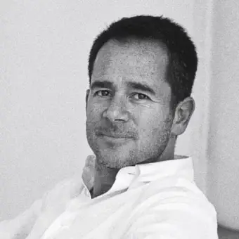 Grayscale portrait of a man with short dark hair and stubble wearing a light collared shirt against a textured light background