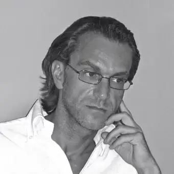 Grayscale portrait of a man with dark hair and glasses looking downward, hand raised to chin, against a plain light gray background