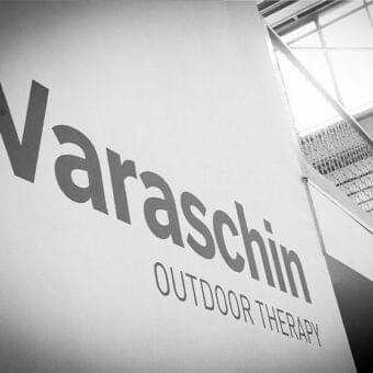 Dark lettering spelling “Varaschin” and “OUTDOOR THERAPY” is displayed on a textured wall beside a diagonally receding metal staircase