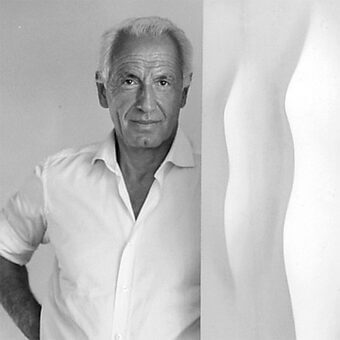 Claudio Lovadina portrait with abstract white sculpture, featuring a curved form and polished surface, against a light neutral wall.