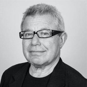 Grayscale portrait of an older man with short gray hair and glasses looking directly at the camera with a slight smile