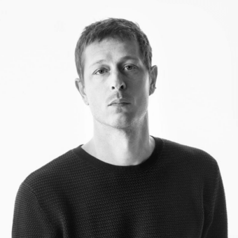 Grayscale portrait of a young man with short dark hair wearing a dark knit sweater against a light gray background